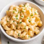 A white bowl of macaroni and cheese next to a fork.