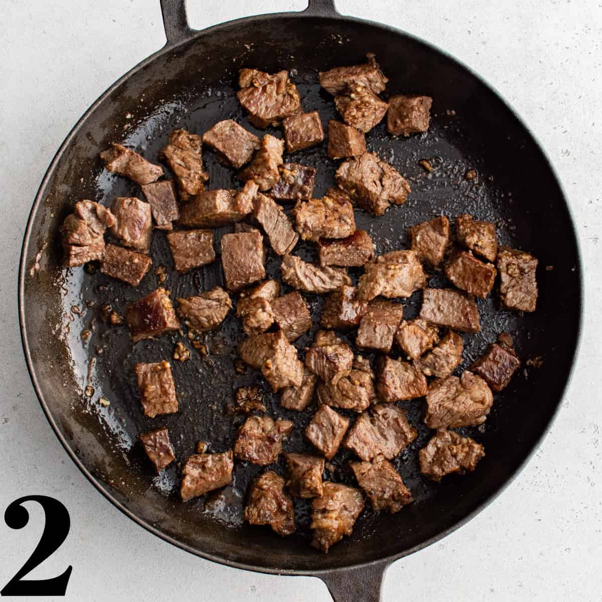 A skillet full of cooked beef chunks.