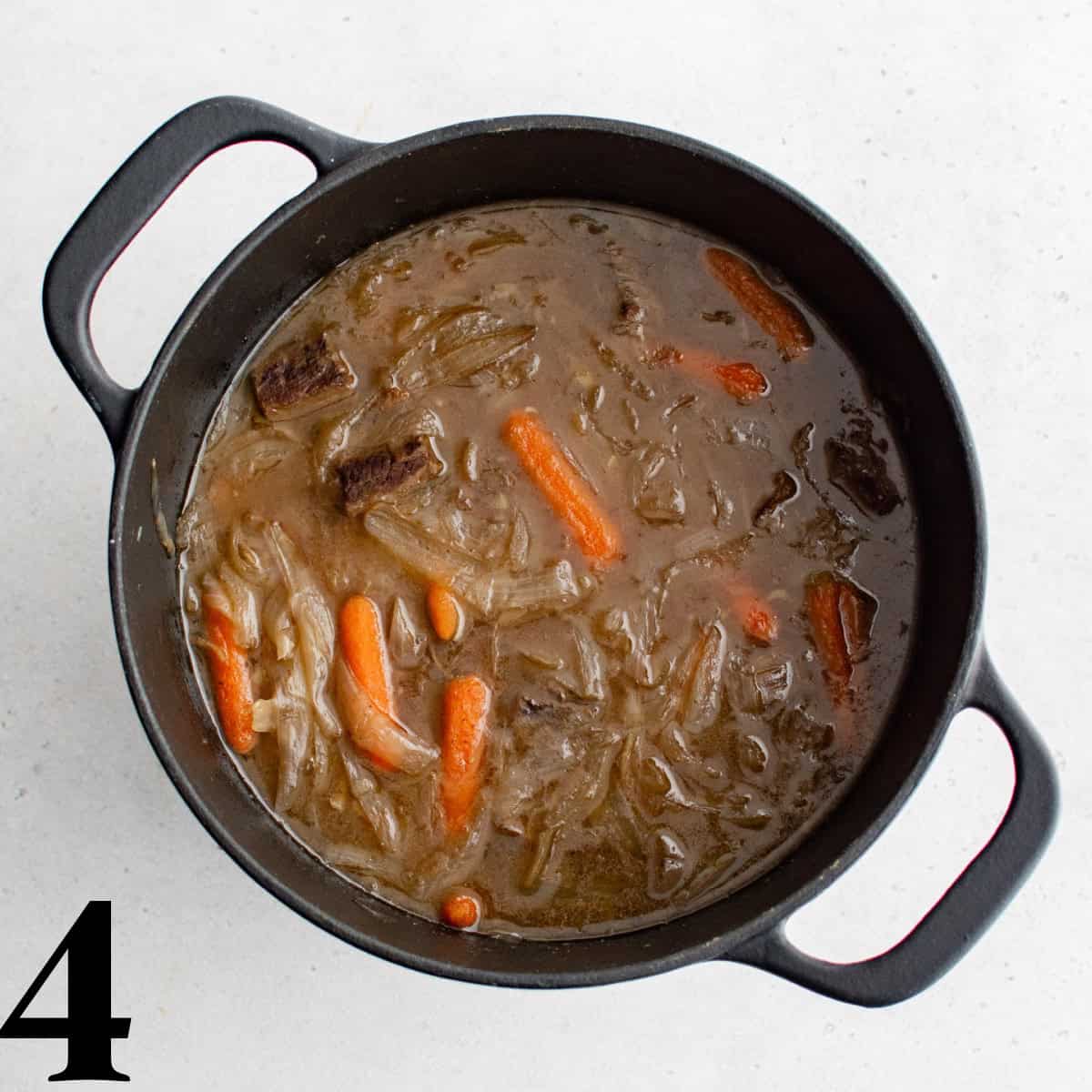 A large pot full of beef stew with carrots.