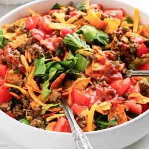 Fresh taco salad with seasoned ground beef, lettuce, tomatoes, shredded cheese, and crispy tortilla chips in a white bowl