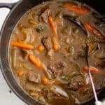 A large pot full of beef stew with carrots.