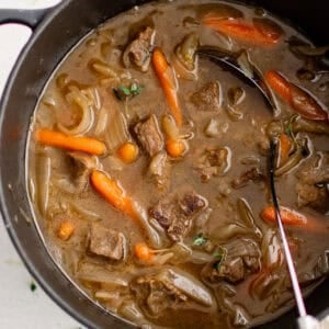 A large pot full of beef stew with carrots.