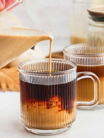 Pumpkin spice coffee creamer being poured into a mug of coffee.