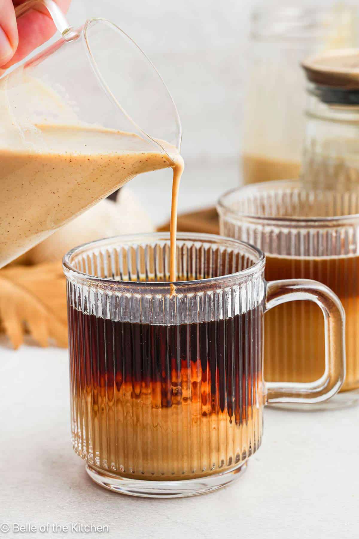 Pumpkin spice coffee creamer being poured into a mug of coffee.