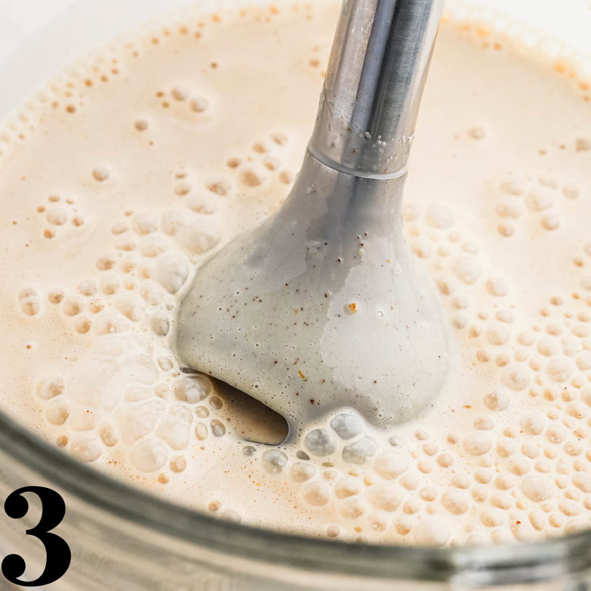 An immersion blender in a bowl of cream.