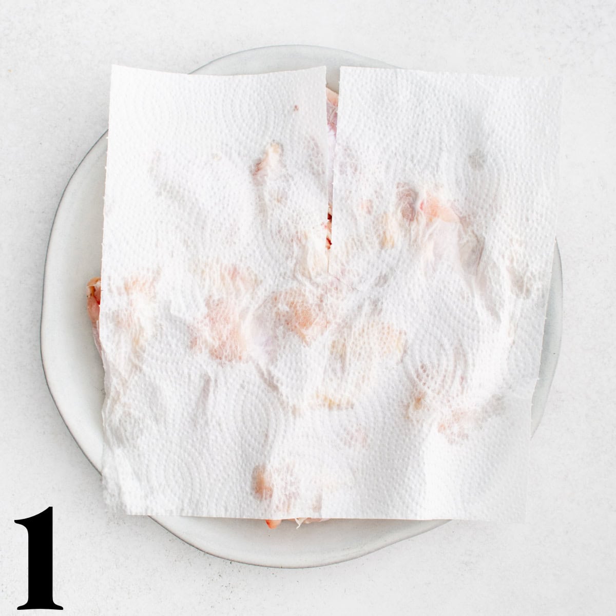 A paper towel blotting chicken wings on a plate.