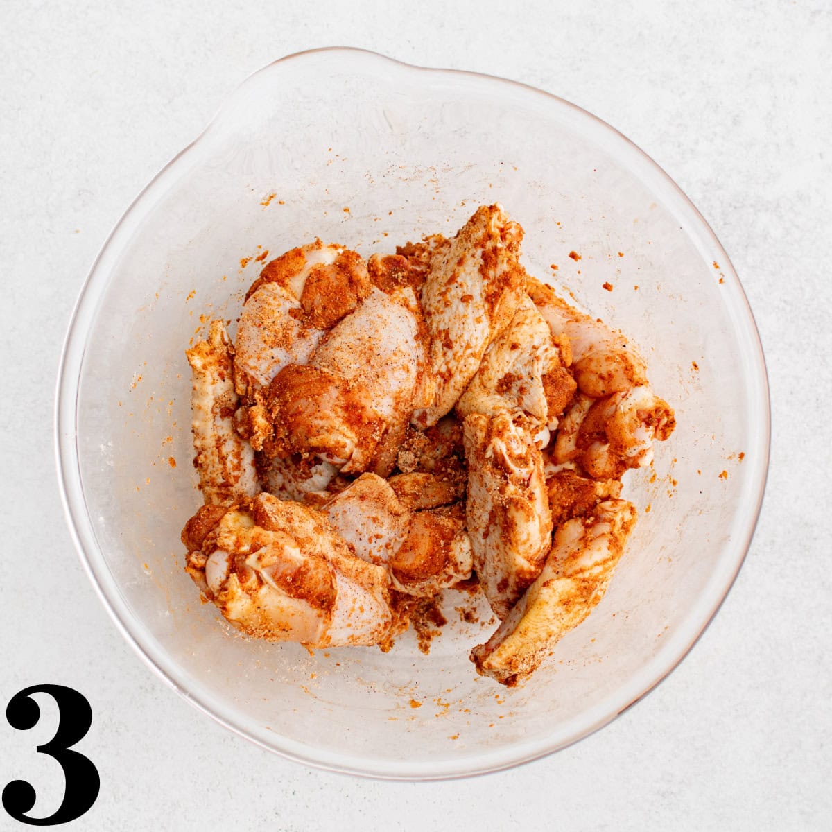 Raw chicken wings in a glass bowl coated with spices.
