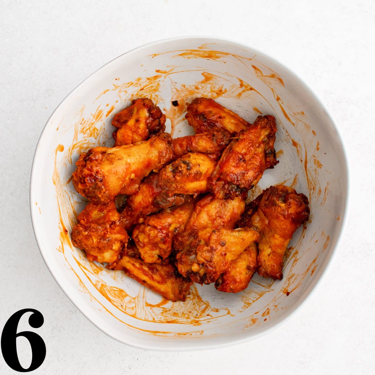 A white bowl of buffalo sauce coated chicken wings.