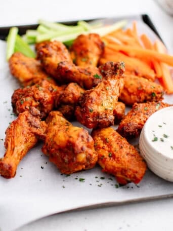 Buffalo wings on a tray with a bowl of ranch, carrots, and celery sticks.