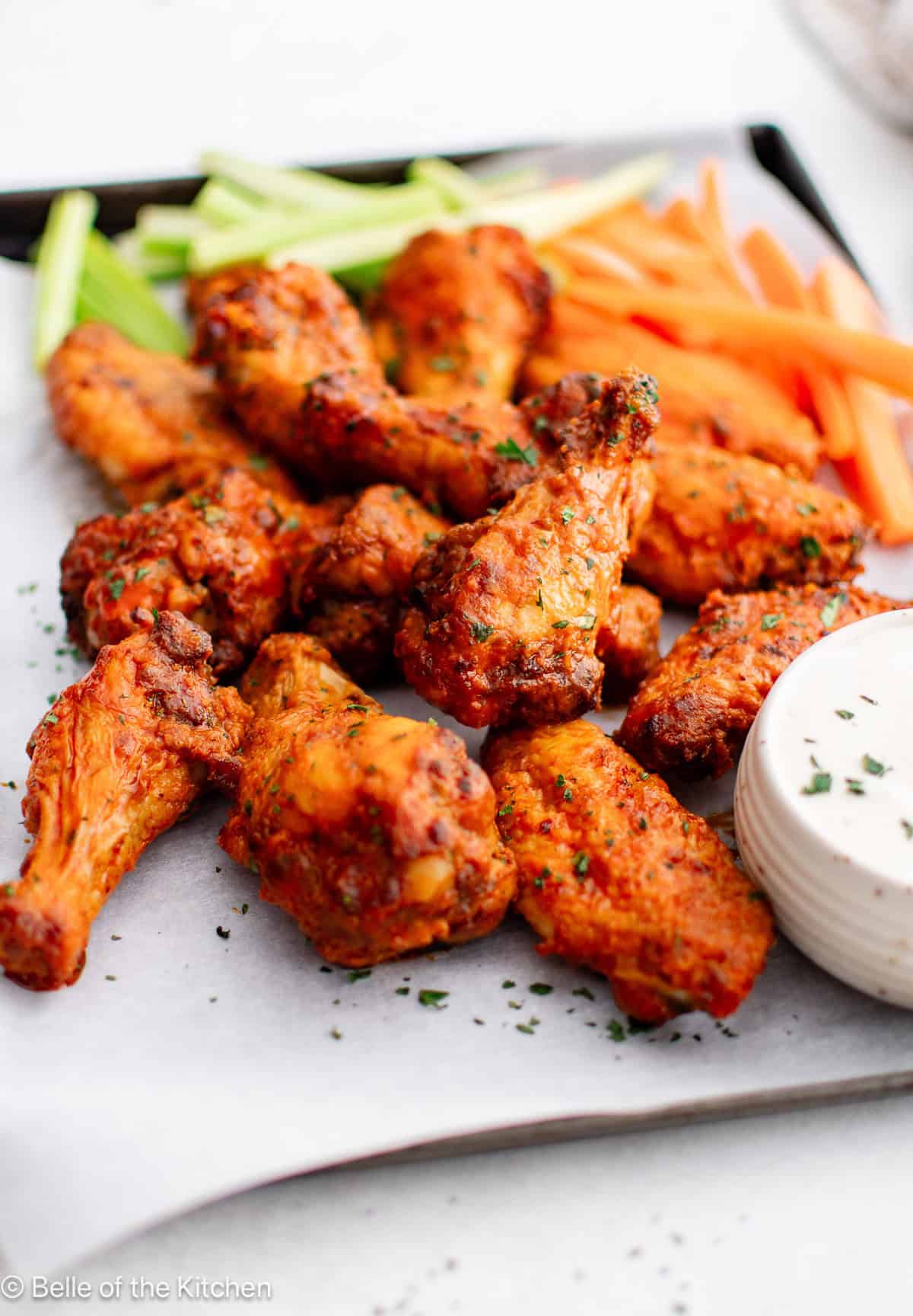 Buffalo wings on a tray with a bowl of ranch, carrots, and celery sticks.