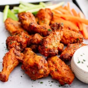 Buffalo wings on a tray with a bowl of ranch, carrots, and celery sticks.
