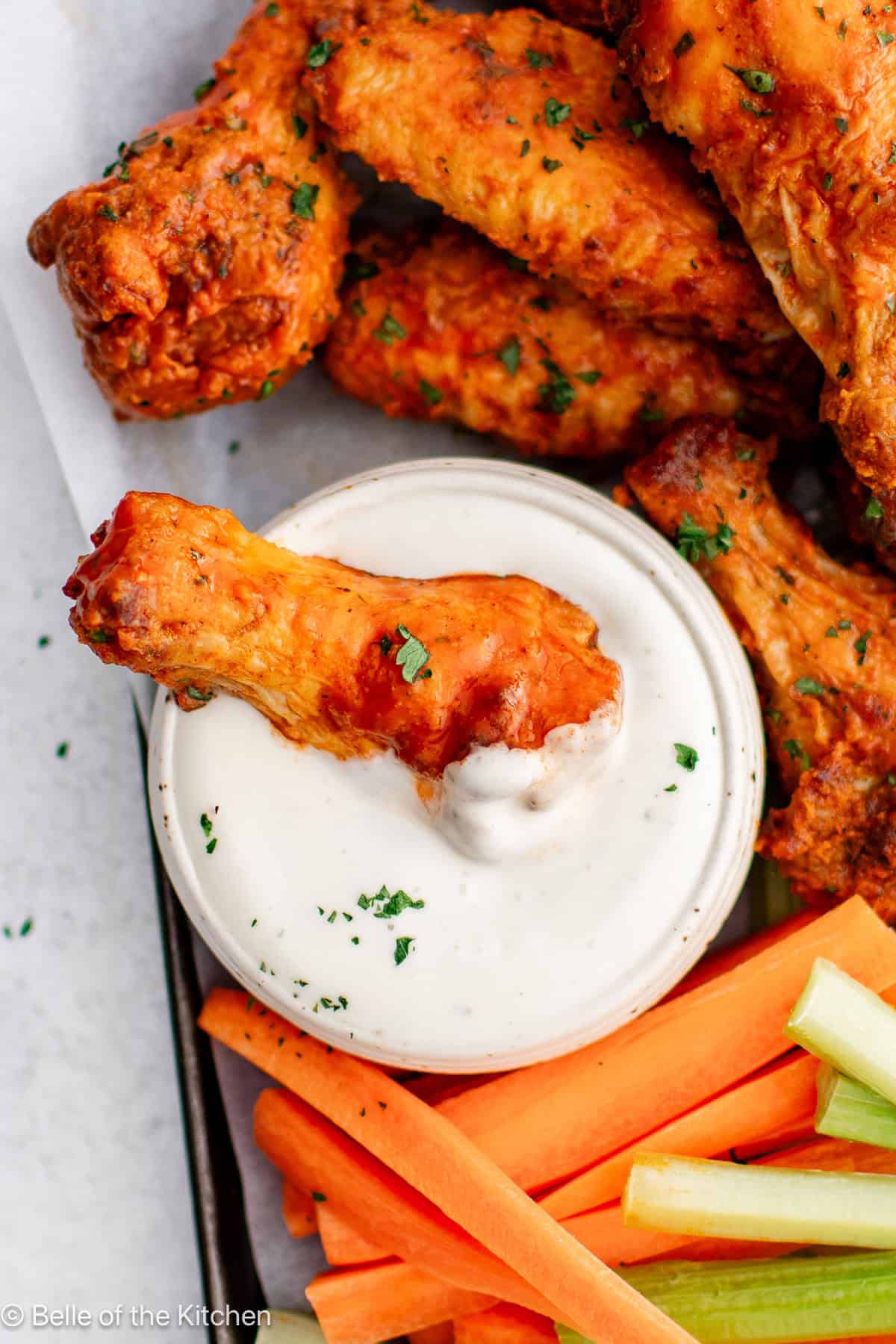 Buffalo wings on a tray with a bowl of ranch, carrots, and celery sticks.