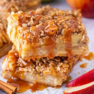 Two slices of apple pie bars stacked with caramel drizzle on top.