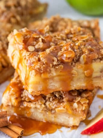 Two slices of apple pie bars stacked with caramel drizzle on top.