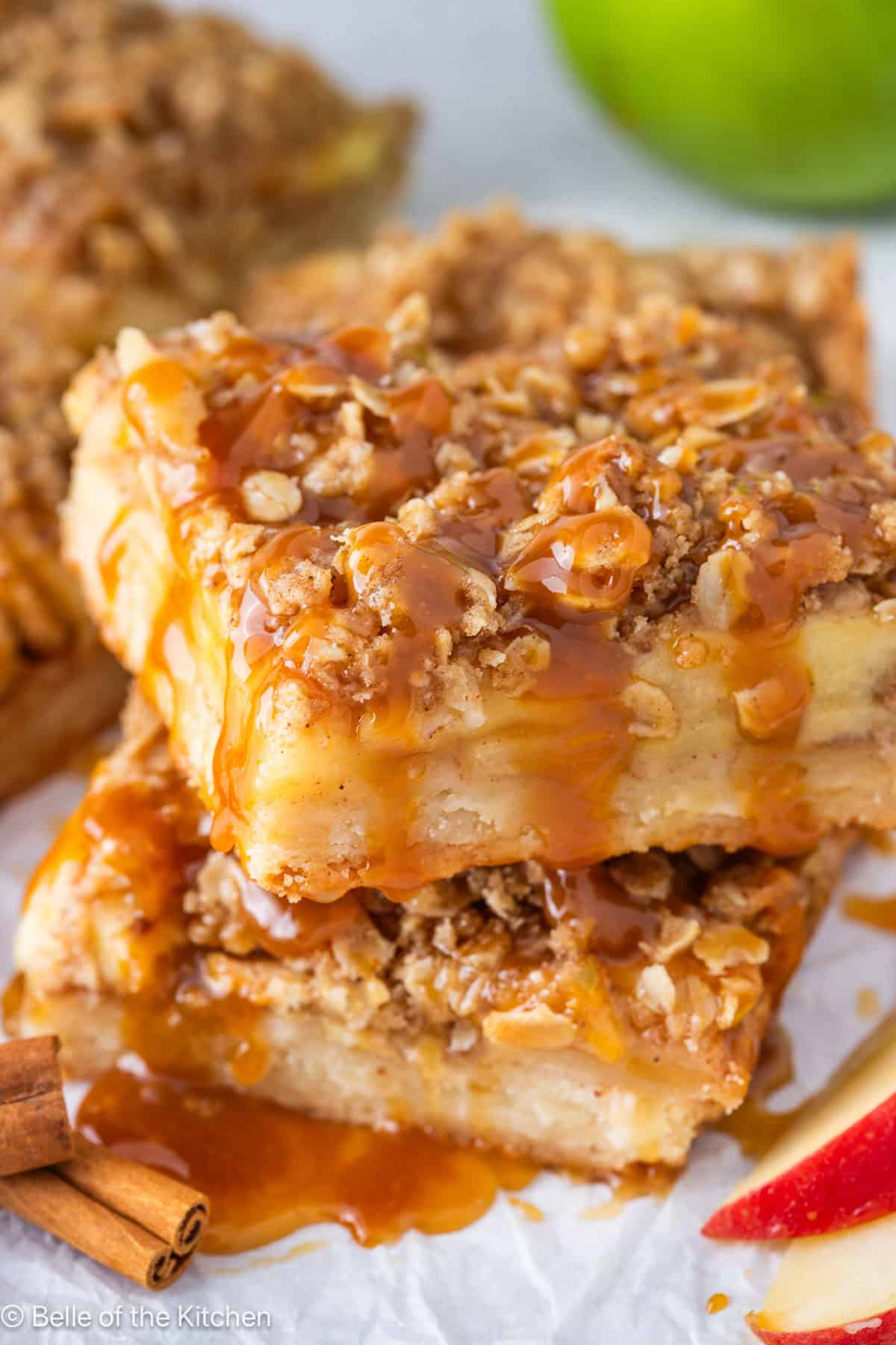 Two slices of apple pie bars stacked with caramel drizzle on top.