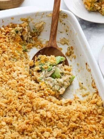 Chicken broccoli rice casserole in a white baking dish with a wooden spoon.