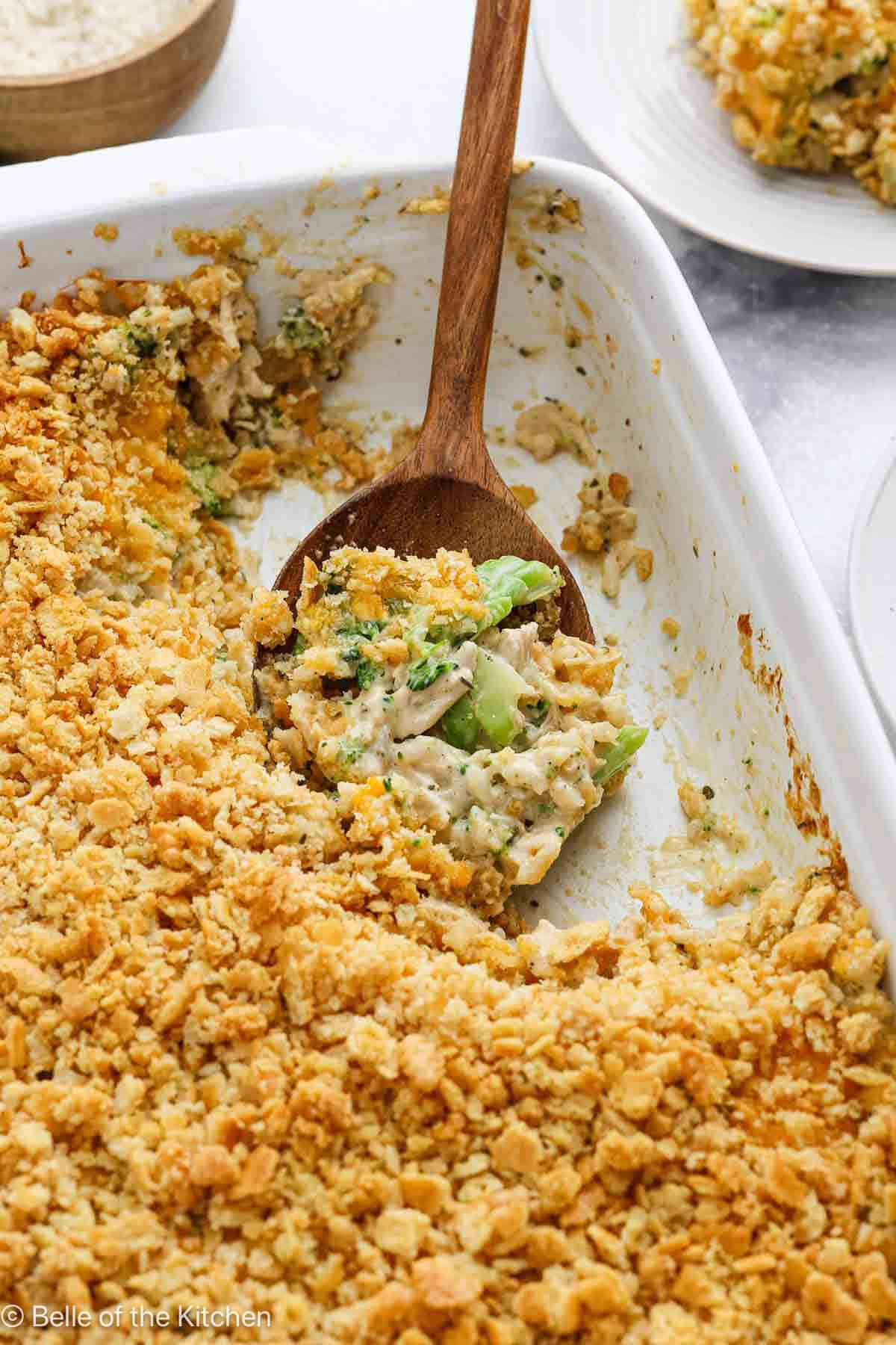 Chicken broccoli rice casserole in a white baking dish with a wooden spoon.
