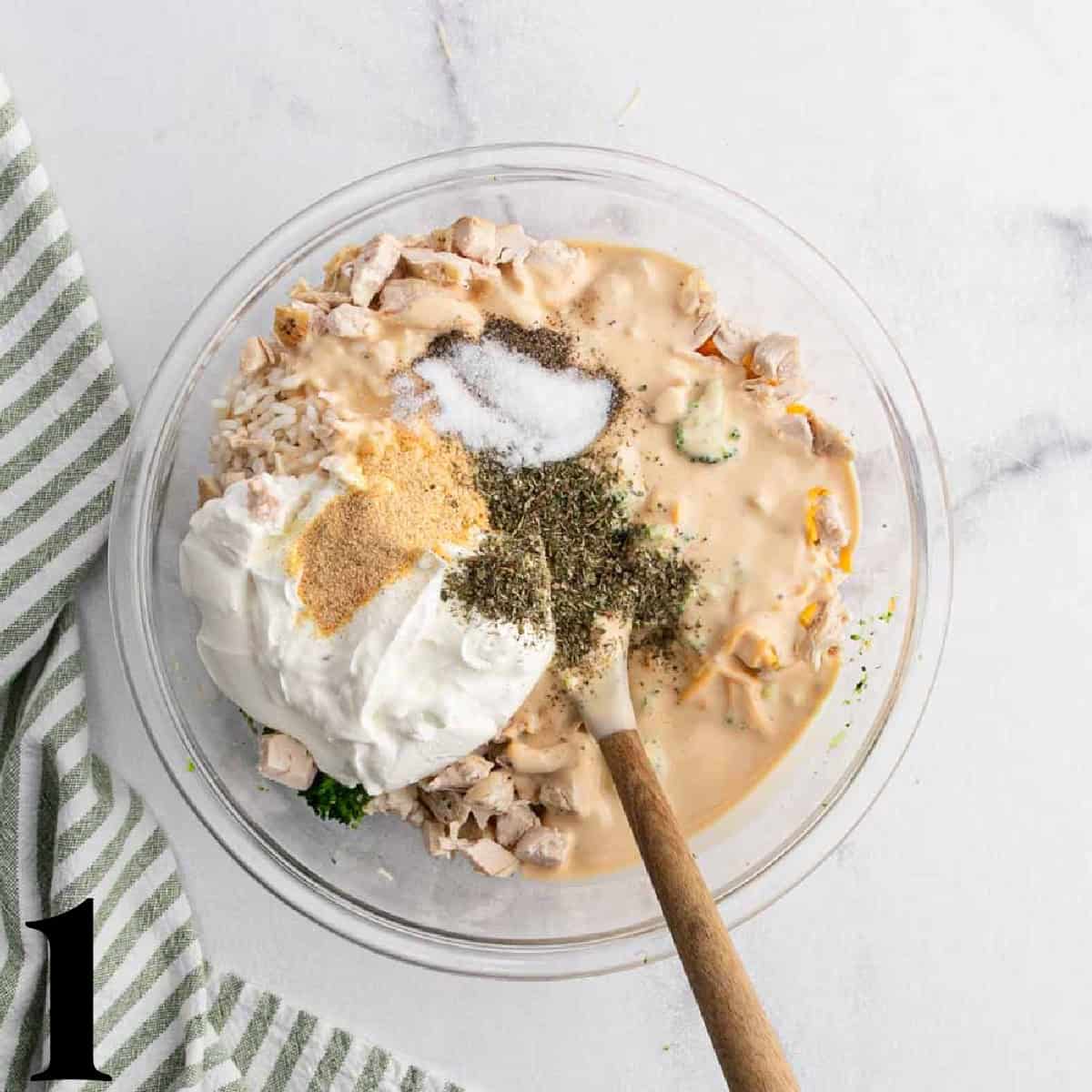 A glass bowl of sour cream, alfredo sauce, spices, and chicken.