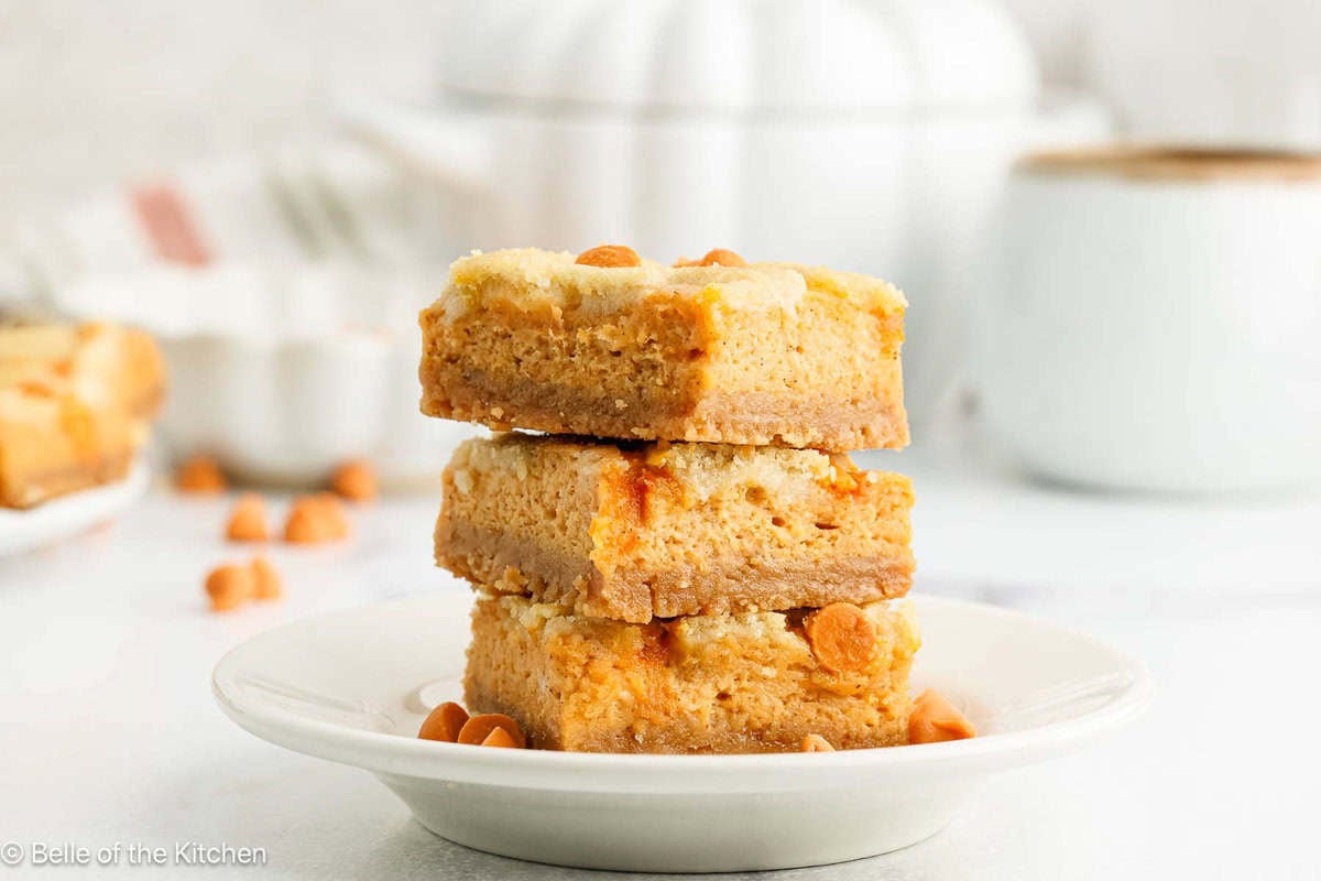 Three pumpkin cheesecake bars stacked on a plate.