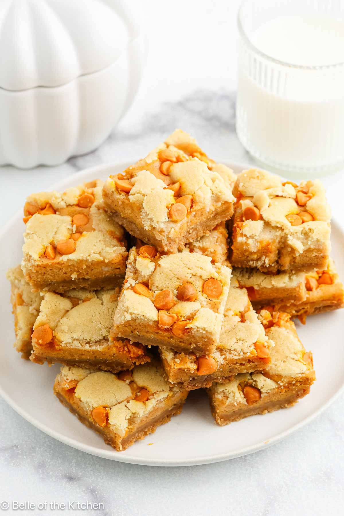 A large stack of pumpkin cheesecake bars on a white plate.