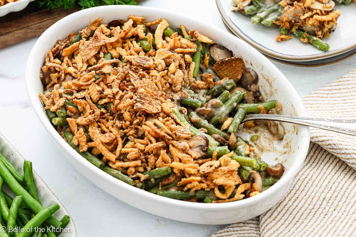 Green bean casserole in a white baking dish with fried green onions on top and a spoon scooping some out.