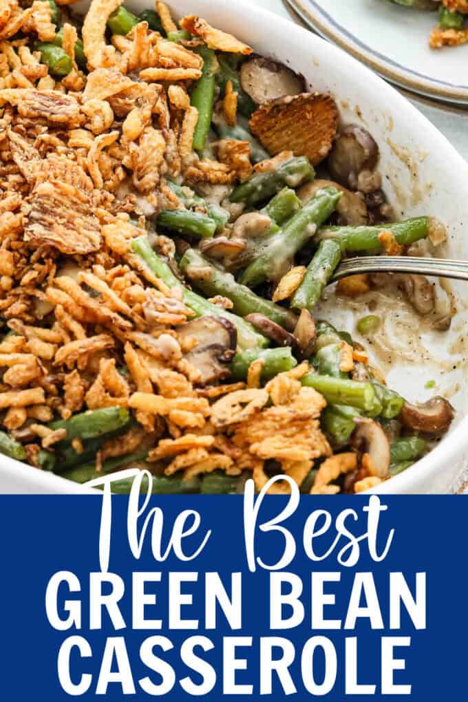 Green bean casserole in a white baking dish with fried green onions on top and a spoon scooping some out.