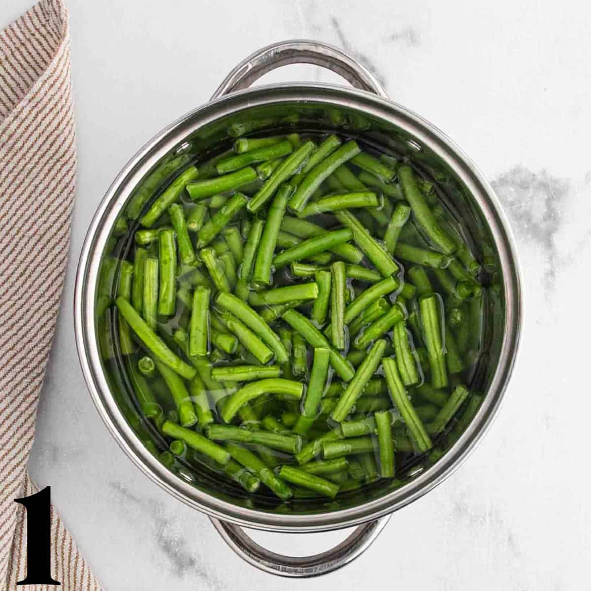 A pot full of green beans in chicken broth.