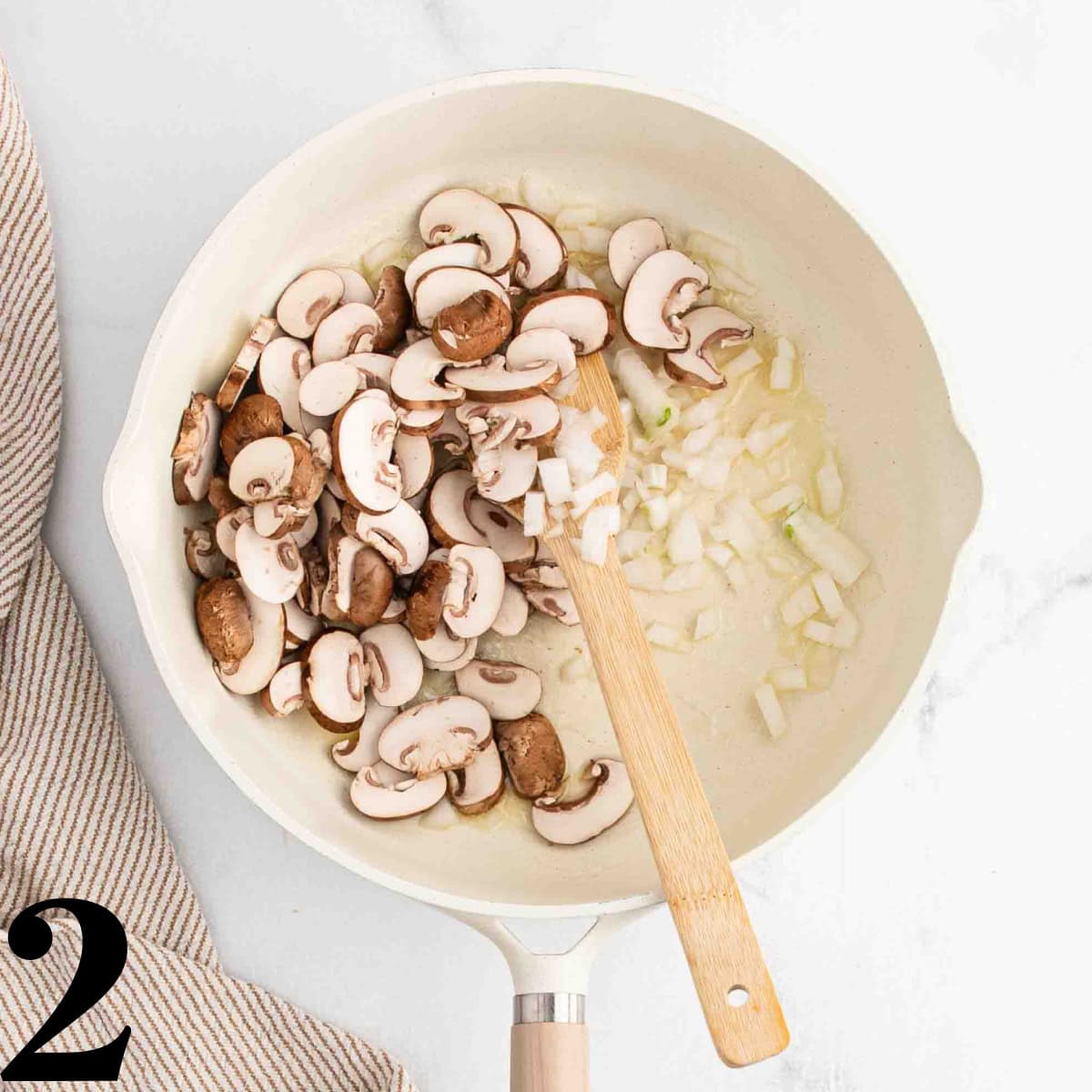 A skillet full of mushrooms and onions with a wooden spoon stirring it.