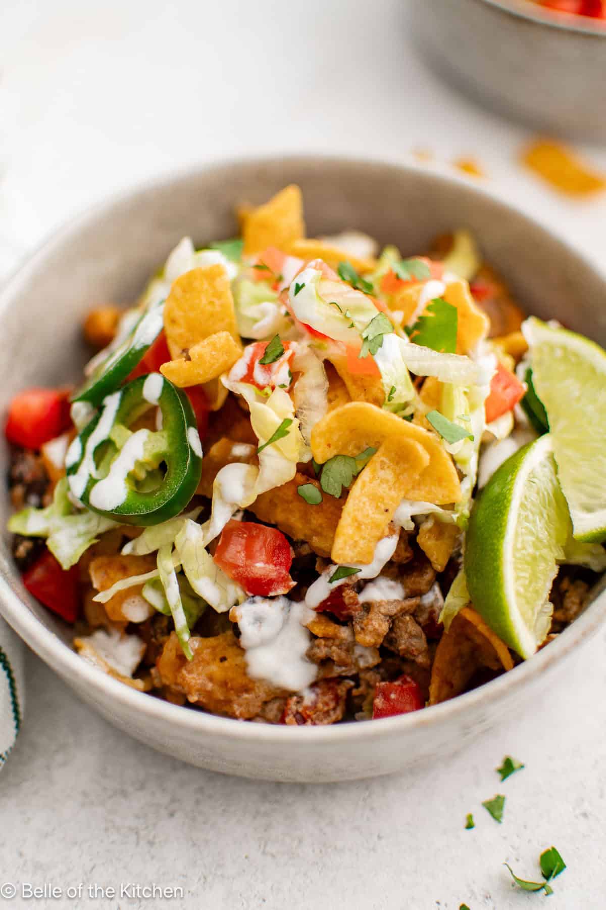 A bowl of taco meat with lettuce, black beans, cheese, tomatoes, and jalapenos.