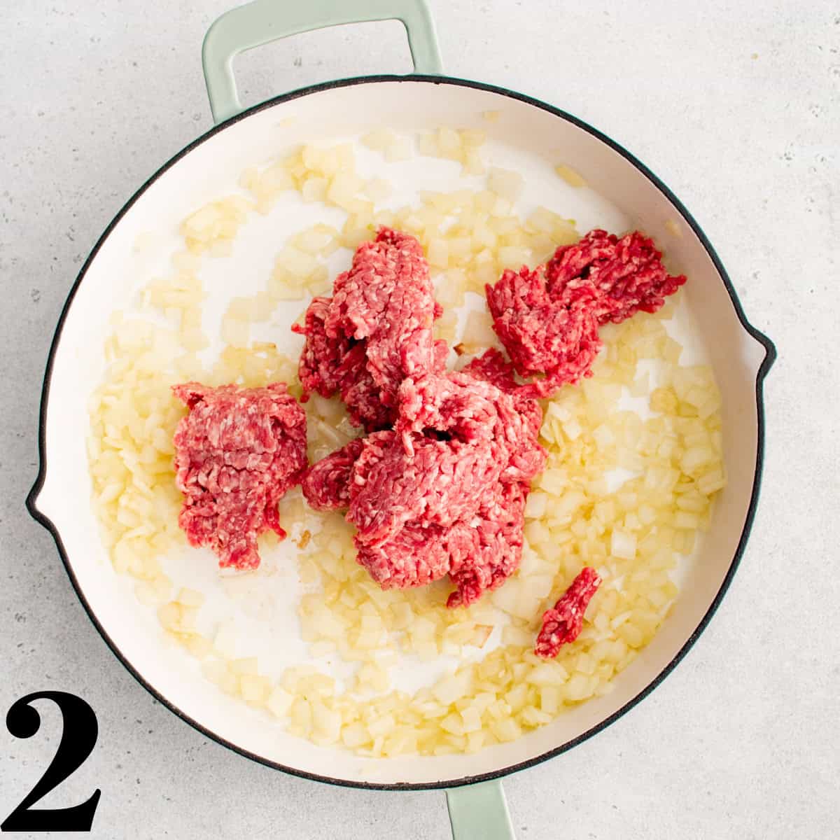 Raw ground beef and onions in a skillet.