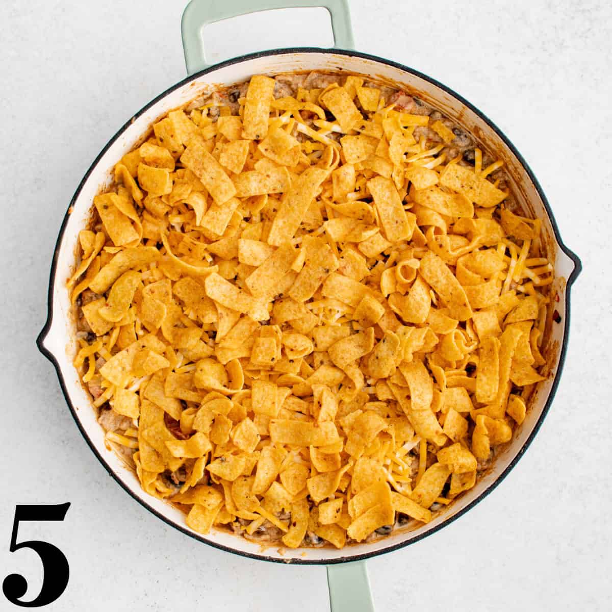 A skillet full of cooked beef with cheese and Fritos on top.