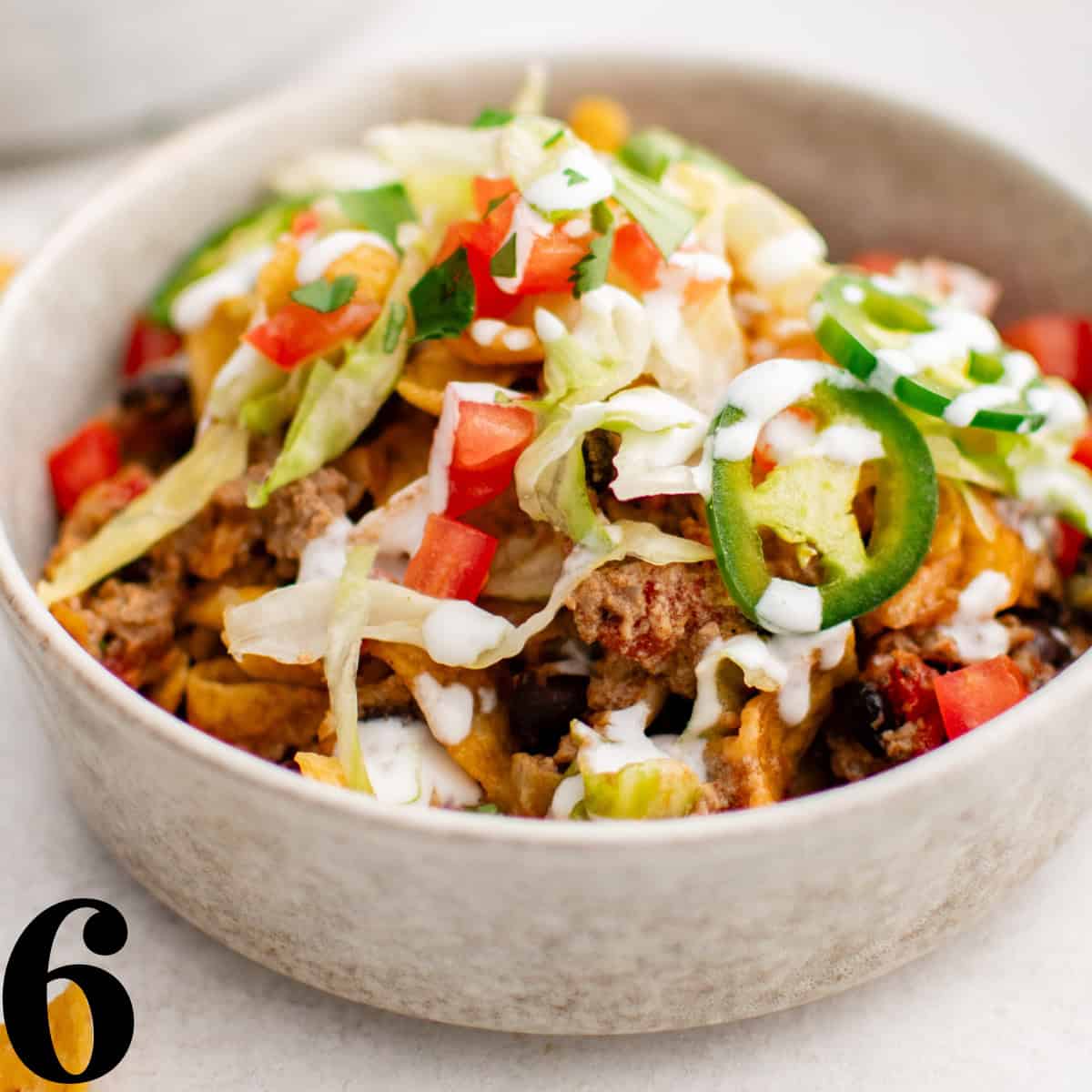 A bowl of taco meat with lettuce, black beans, cheese, tomatoes, and jalapenos.