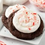 Chocolate cookies topped with frosting and crushed candy canes on a white plate.