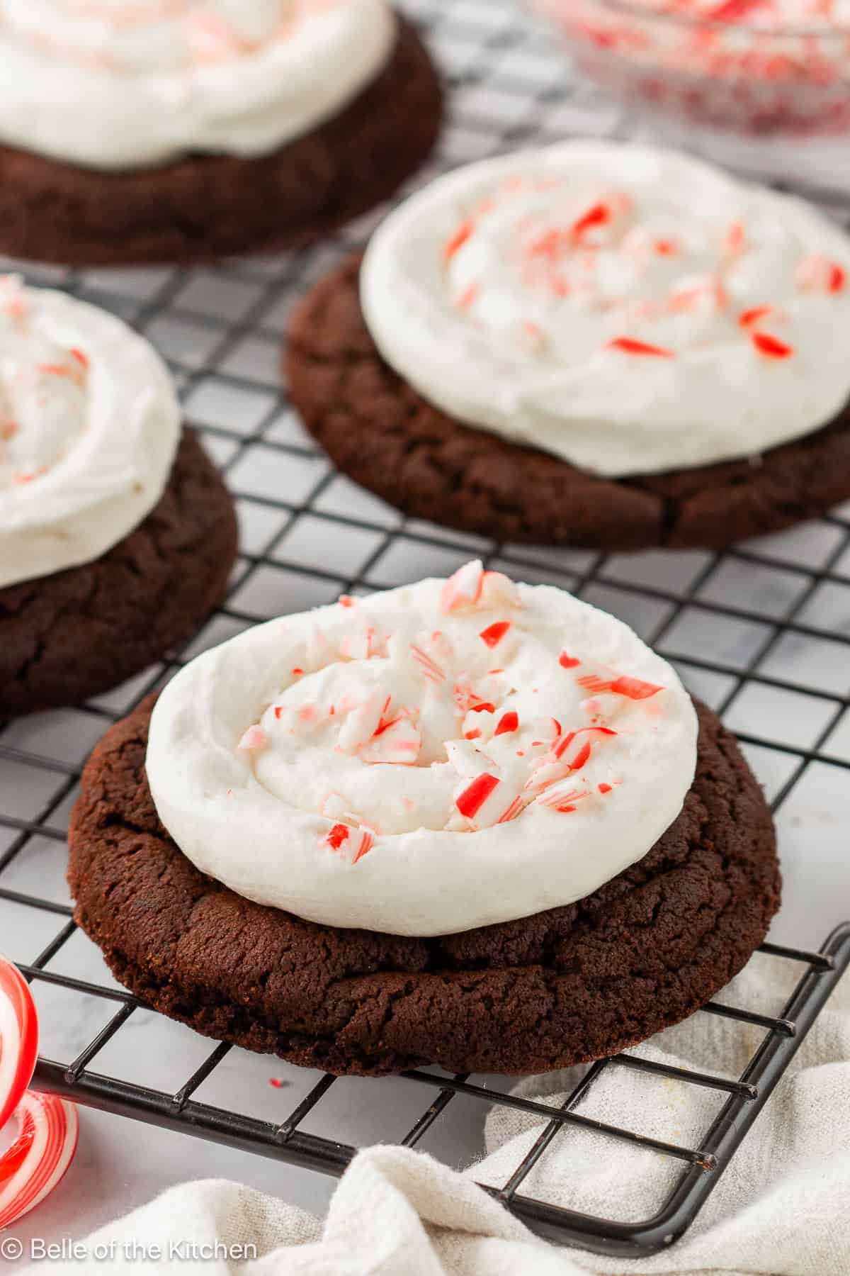 Chocolate cookies topped with frosting and crushed candy canes on a wire rack.