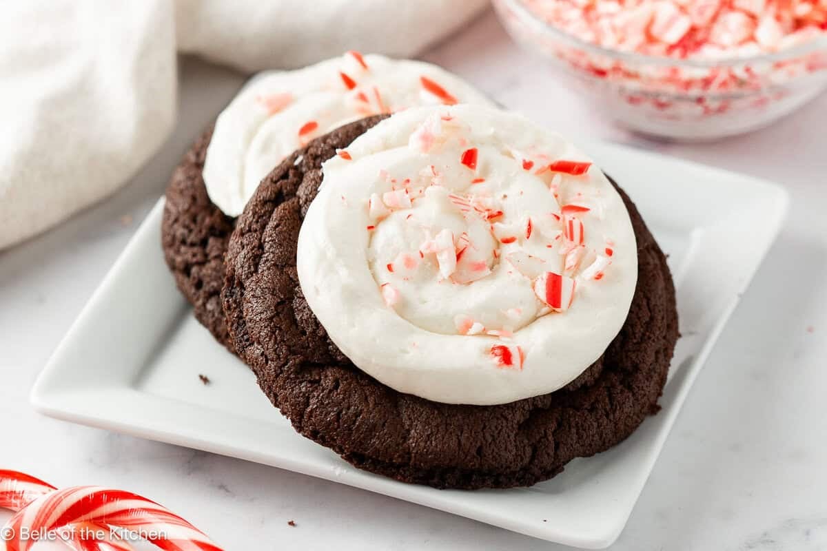 Chocolate cookies topped with frosting and crushed candy canes on a white plate.