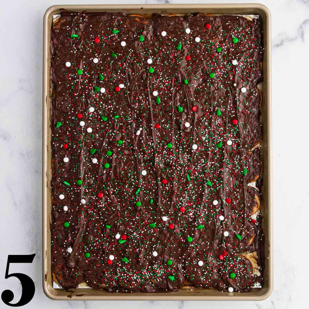Chocolate and sprinkles on top of Ritz crackers on a cookie sheet.
