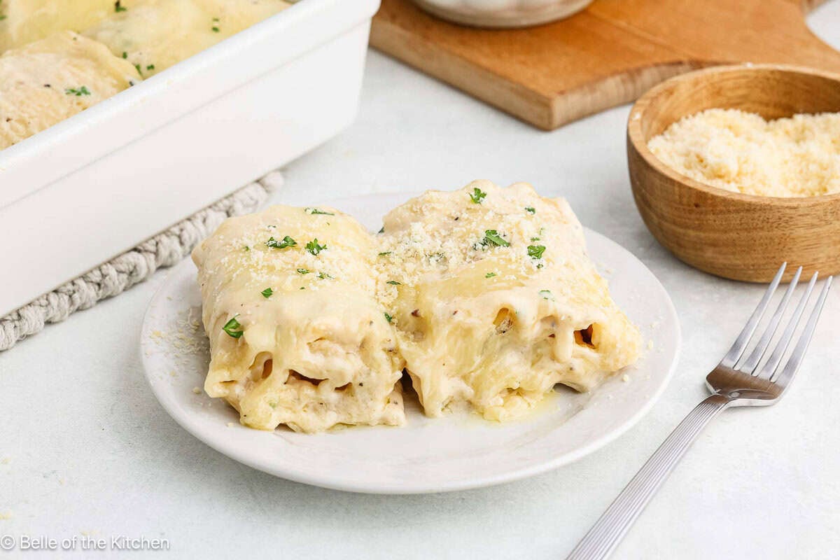 A white plate holding two chicken alfredo lasagna roll ups.