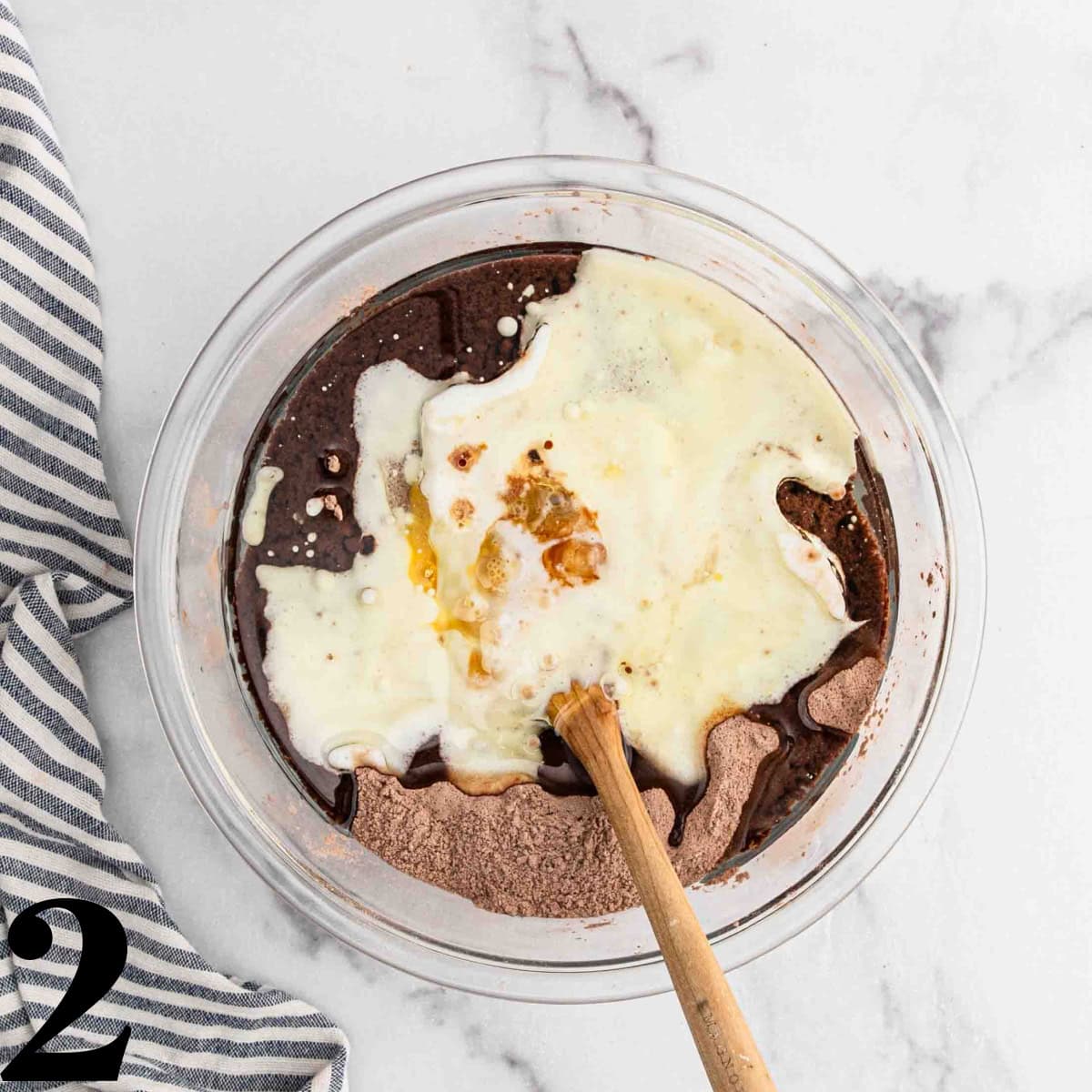 A glass bowl full of sugar, flour, and cocoa powder with a wooden spoon.