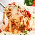 A spoon scooping up baked pasta from a baking dish.