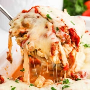 A spoon scooping up baked pasta from a baking dish.