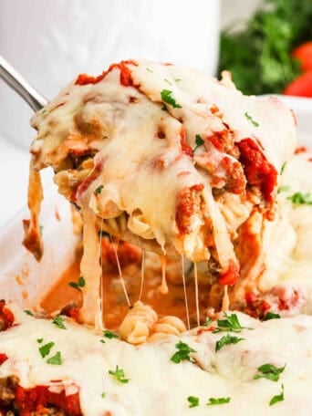 A spoon scooping up baked pasta from a baking dish.