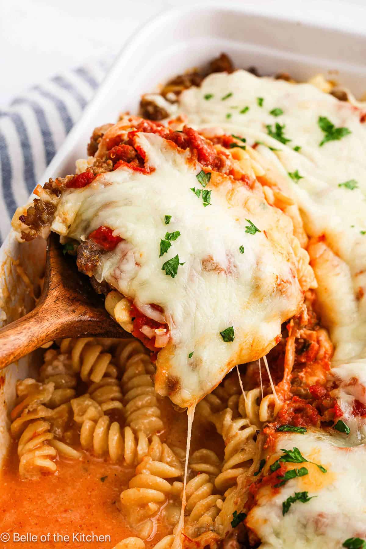 A spoon scooping up baked pasta from a baking dish.
