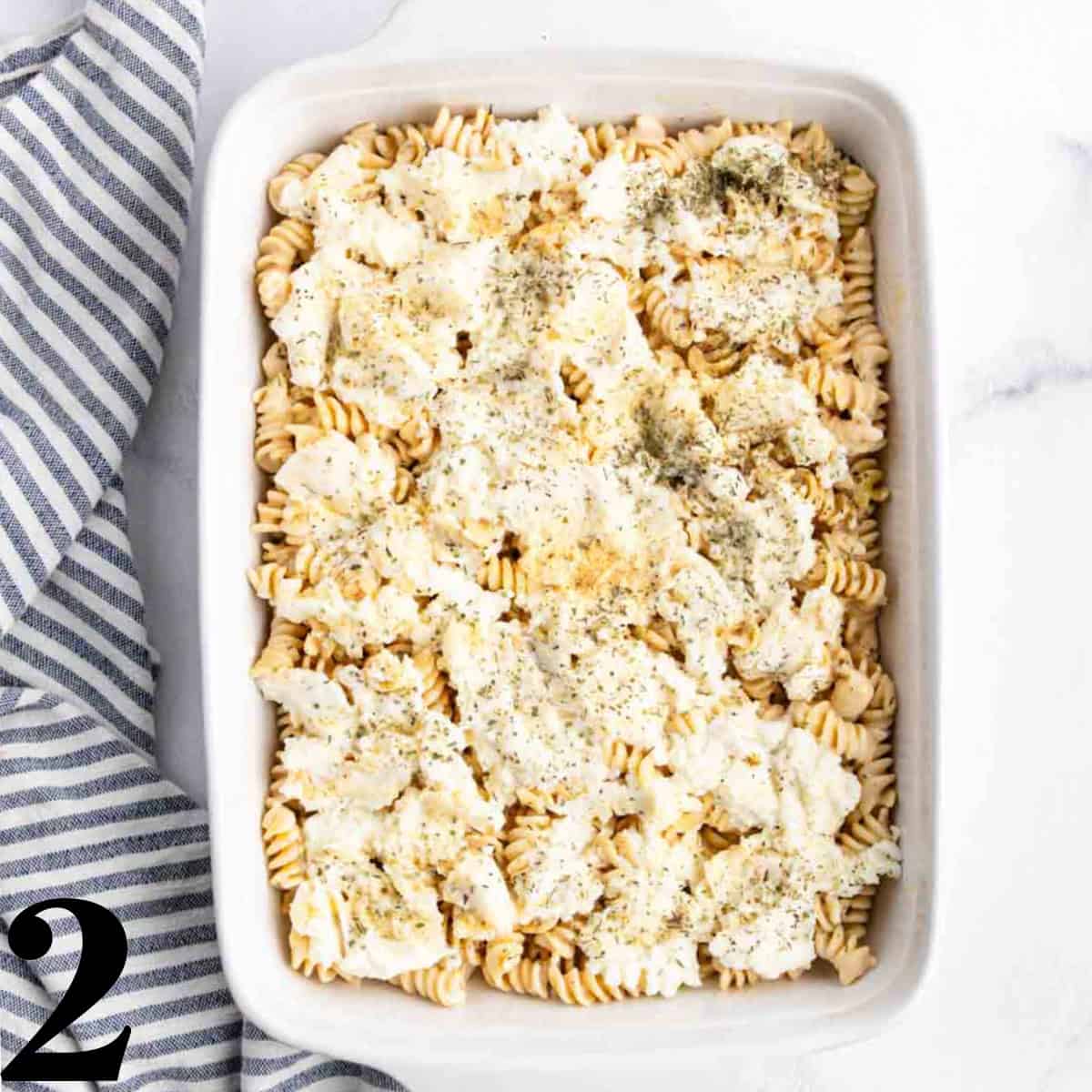 Pasta inside of a white baking dish with ricotta cheese spread on top.