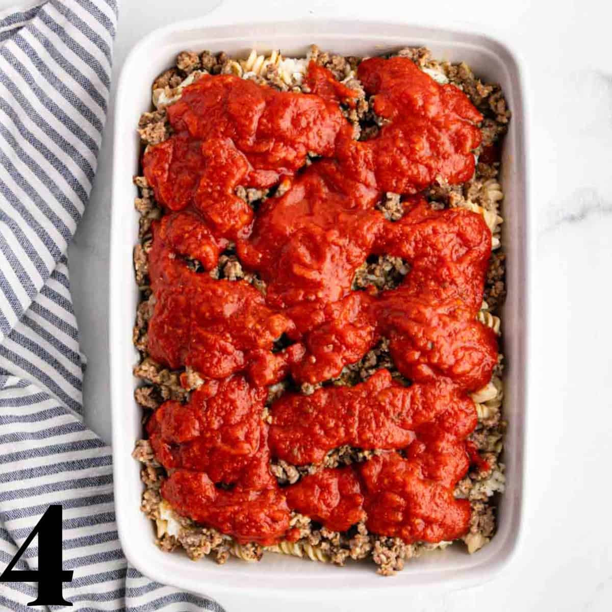 Marinara sauce on top of pasta in a white baking dish.