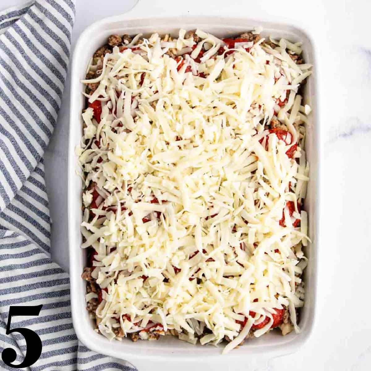 Cheese on top of pasta in a white baking dish.