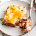 A white plate with a square piece of cowboy casserole on it with a fork.