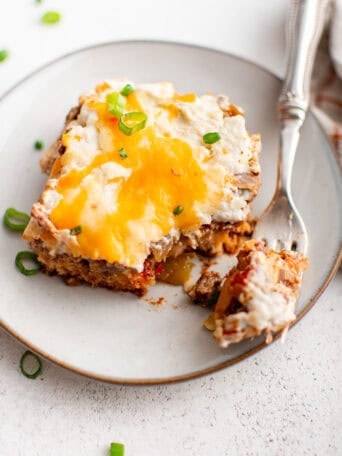 A white plate with a square piece of cowboy casserole on it with a fork.