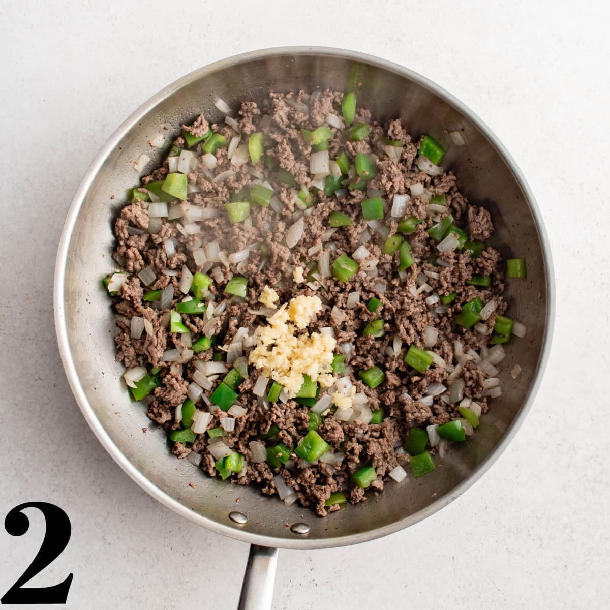 A skillet containing cooked ground beef, onions, green pepper, and garlic.