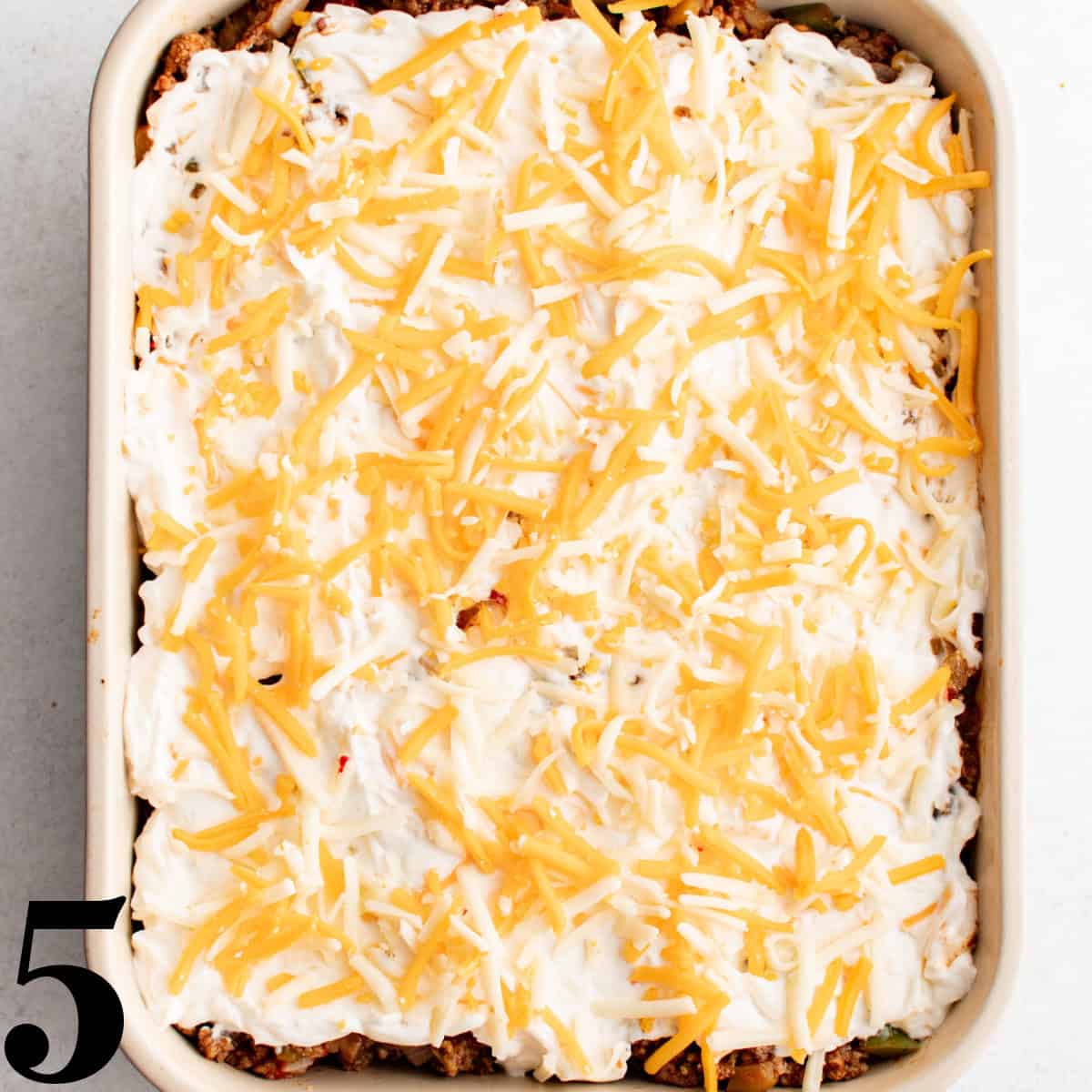 A white baking dish containing cowboy casserole with cheese on top.