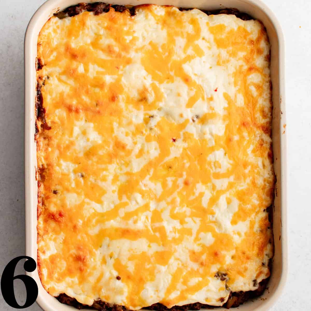 A white baking dish containing cowboy casserole with melted cheese on top.